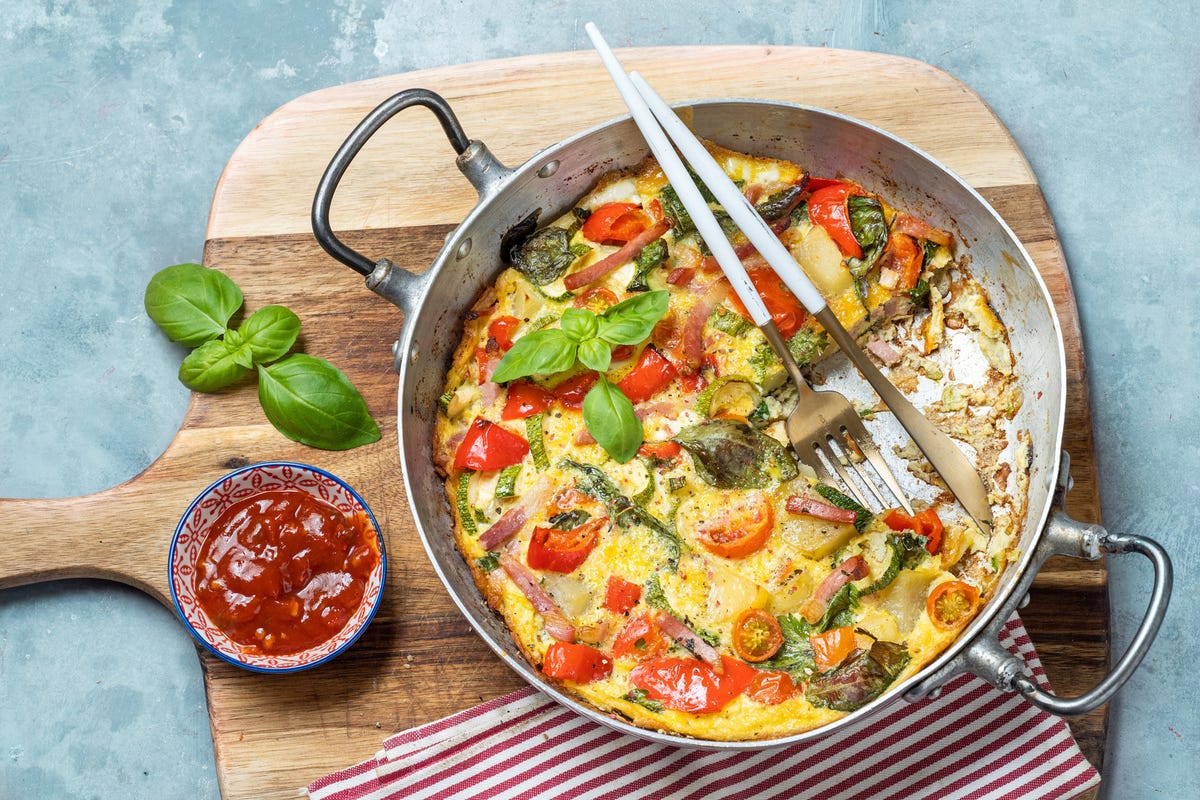 Una frittata fatta con uova e verdure cotte al forno su una padella padella  tagliato a metà per servire sul piano di cottura a gas Foto stock - Alamy