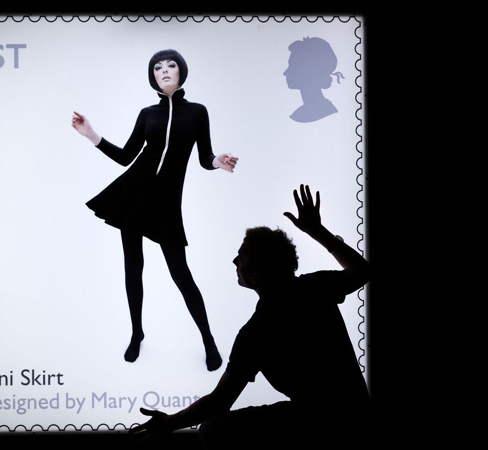 an oversized reproduction of a postage stamp made for mary quant, a woman stands in the middle of the stamp with a swinging jersey dress and tights