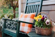 front porch ideas close up of a basket filled with pansies next to a green rocking chair on a patio