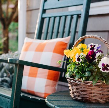front porch ideas close up of a basket filled with pansies next to a green rocking chair on a patio