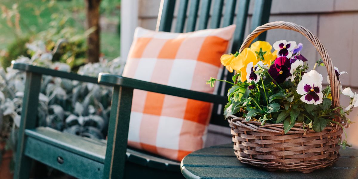 front porch ideas close up of a basket filled with pansies next to a green rocking chair on a patio