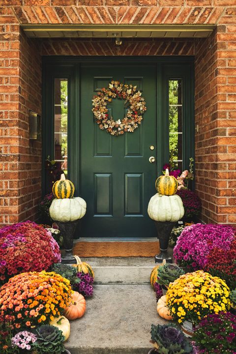 dark green front door with brick around it and pumpkins, planters of mums and gourds leading up to the door