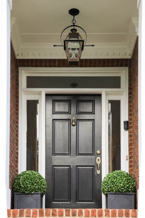 brick front stoop with black door, topiary greenery in square black pots on either side of the door and a french quarter style yoke lantern hanging from the ceiling