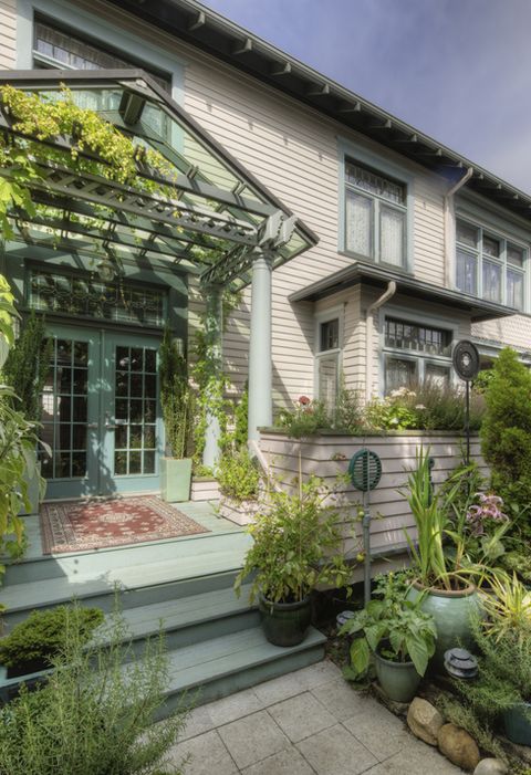 porch with pergola overtop of it with plants wining through it, a rug on the floor and plants in planters alongside the door and steps