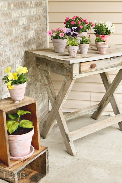 front porch with an old, distressed table with flowers in whitewashed pots on top of it and a couple of old wood crates with more flowers in whitewashed pots