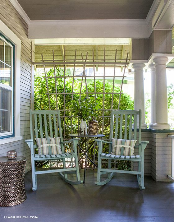 porch with two light green rockers with striped pillows sitting side by side with a small round table with a jar and a vase with greenery sitting in between them