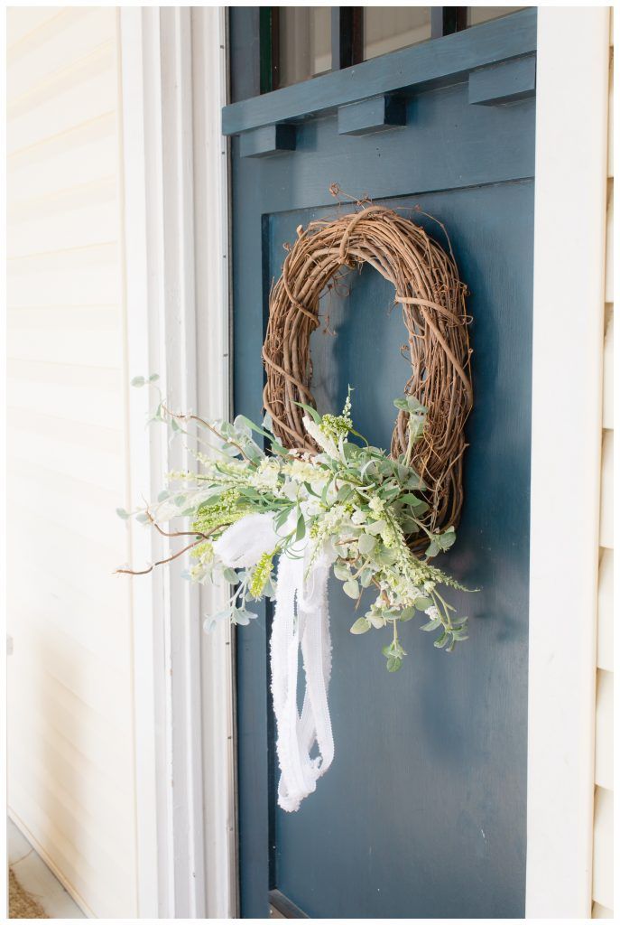 side view of blue front door with grapevine wreath on it with white and yellow spring wildflowers and a white fabric bow