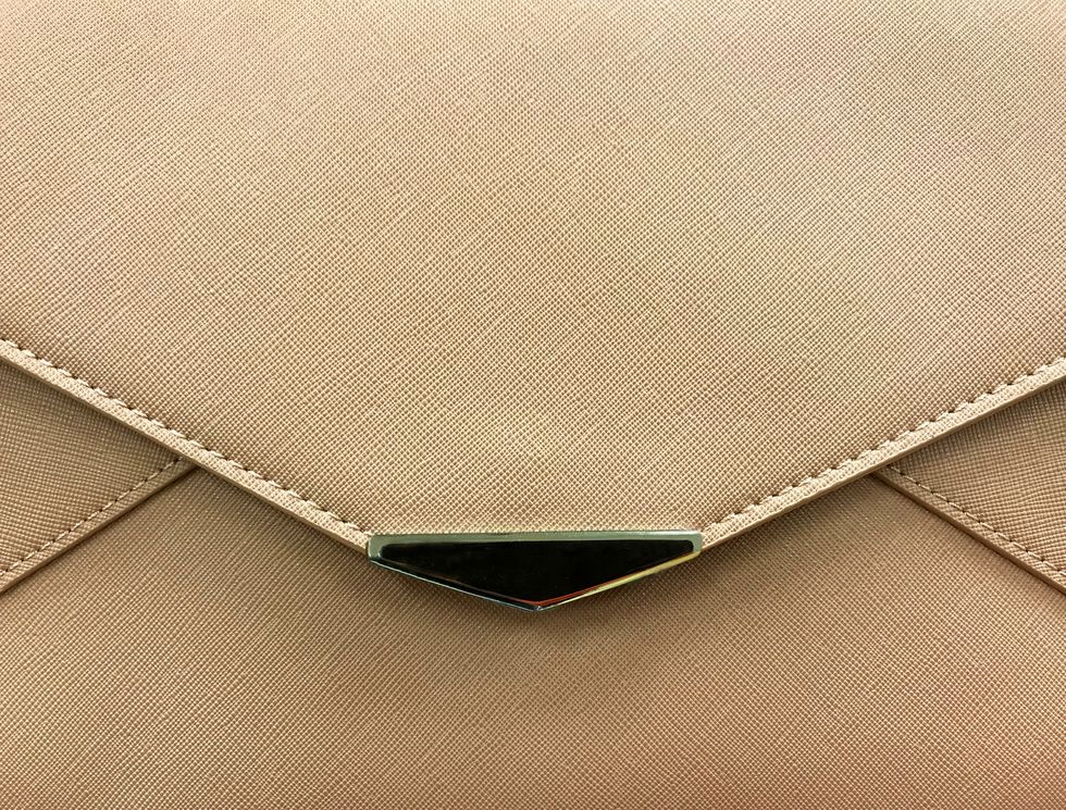 Front view of a light brown purse showing edge of flap and metal decor