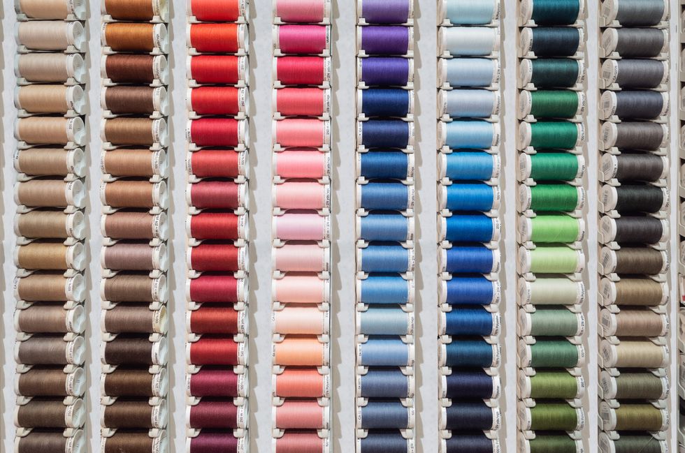front view of a many spools of thread of different colors displayed in a store for sale.