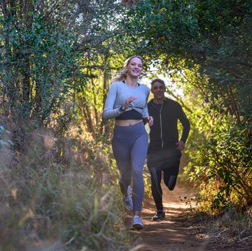 front view young couple racing through forest on footpath sprinting over rough terrain