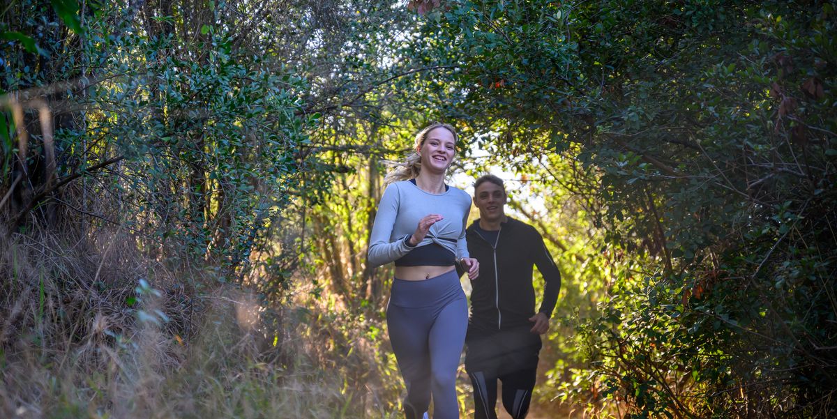 front view young couple racing through forest on footpath sprinting over rough terrain