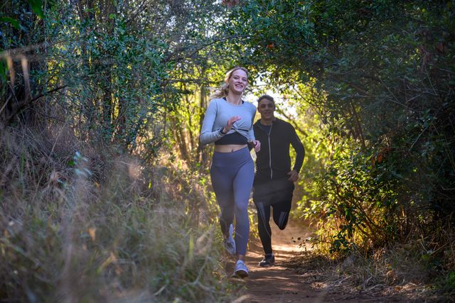 front view young couple racing through forest on footpath sprinting over rough terrain