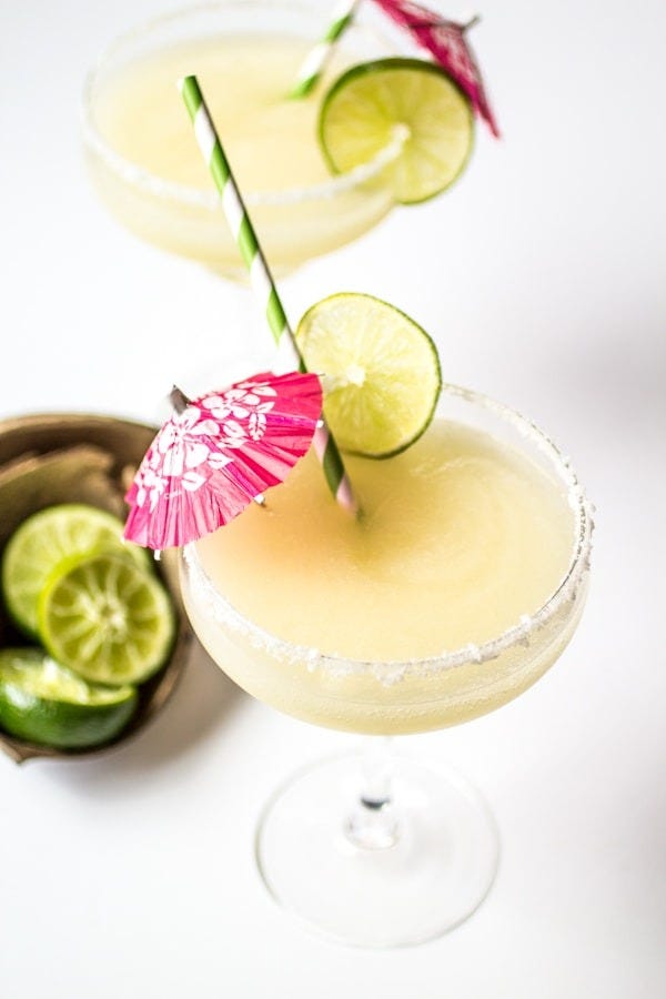 frozen coconut margaritas with slices of lime for garnish and drink umbrellas and paper straws