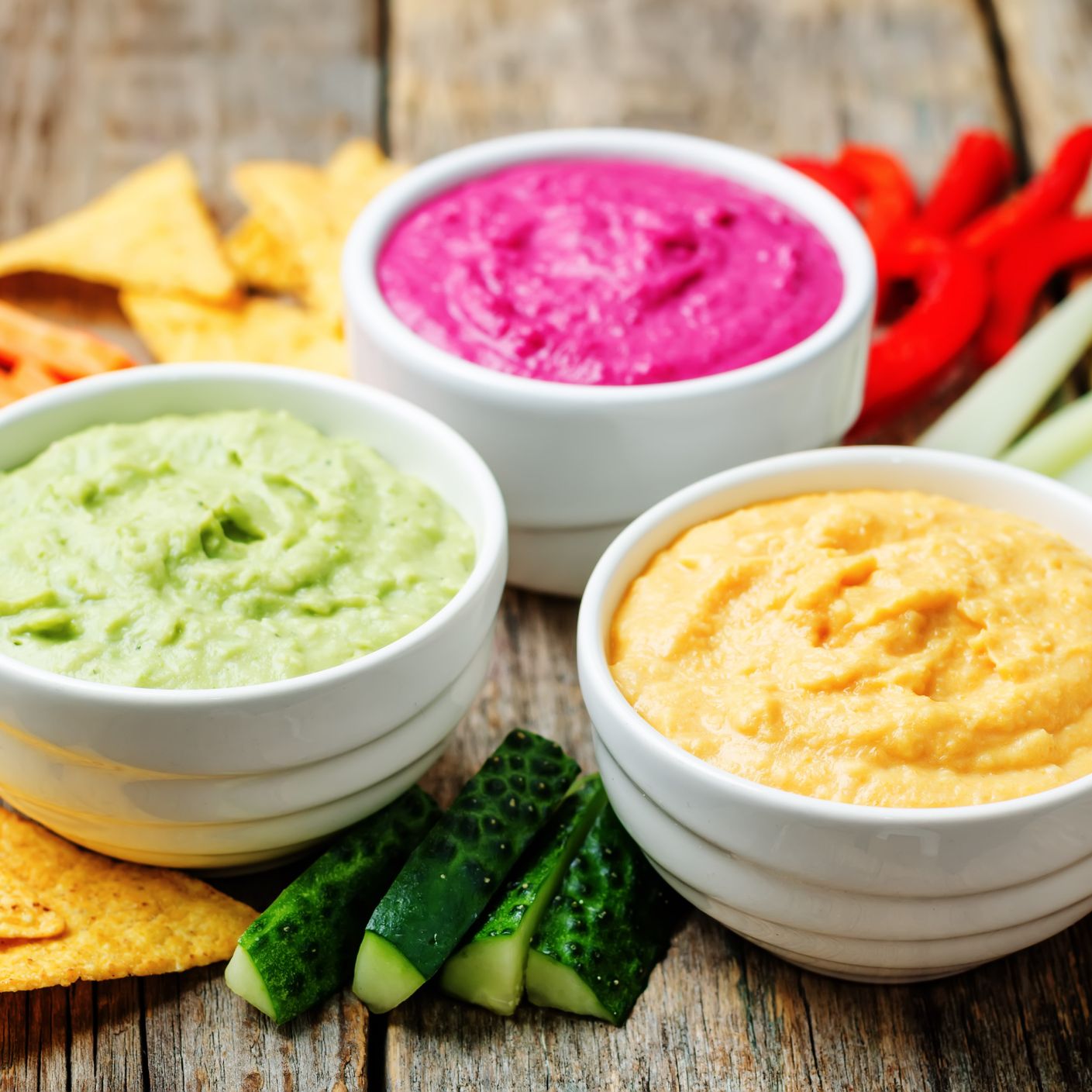 guacamole, hummus, and pink dip surrounded by veggies and tortilla chips