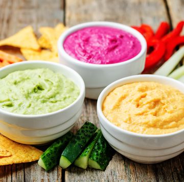 guacamole, hummus, and pink dip surrounded by veggies and tortilla chips