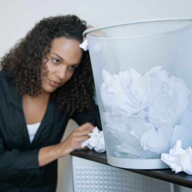 frustrated businesswoman with wastebasket full of paper wads