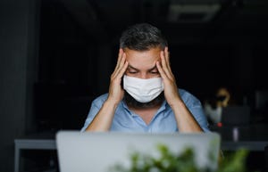 frustrated mature man with face mask sitting indoors in office, working