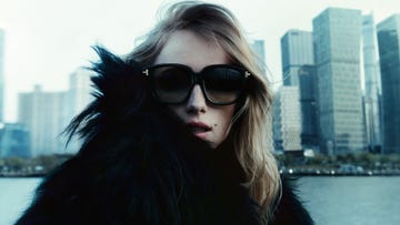 person wearing a black fur coat with city skyline in the background