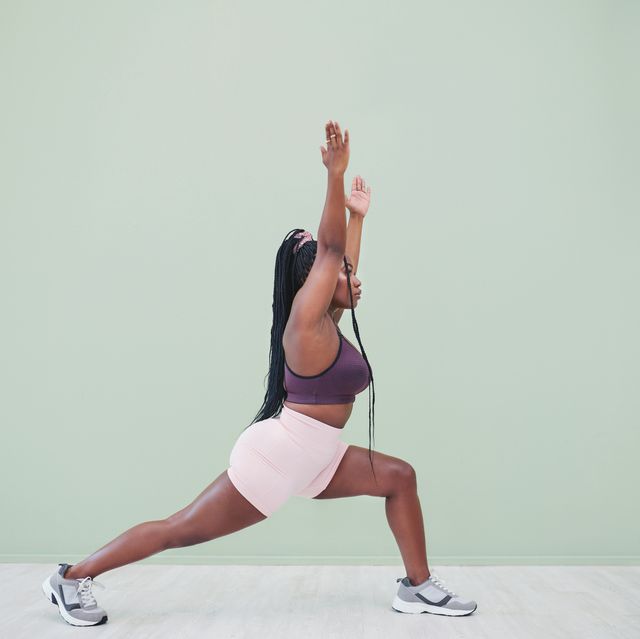 full body studio shot of a young woman exercising against a green background
