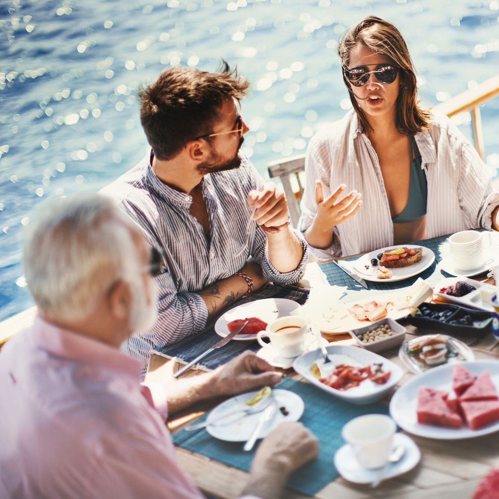 three people gathered around a table with food on a sunny cruise ship