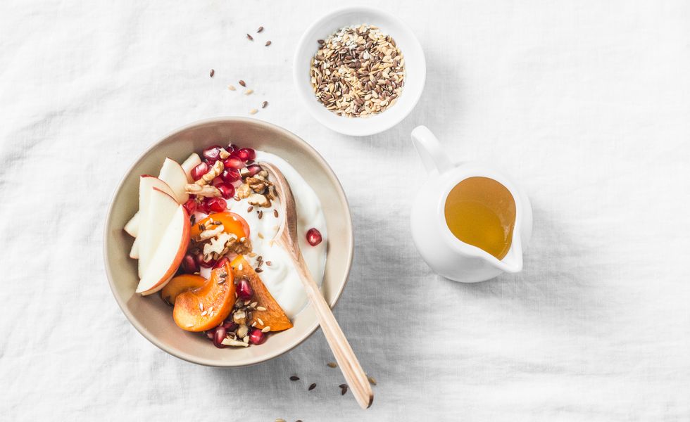 Full fruit and greek yogurt breakfast bowl. Persimmon, apple, walnuts, pomegranates and natural yogurt. Healthy food concept on light background, top view