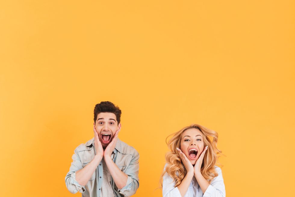 full length image of happy couple shouting and touching cheeks while jumping with spreading legs, isolated over yellow background