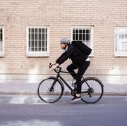 full length of businessman cycling on street by building in city
