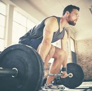 full length of confident man dead lifting barbell in gym