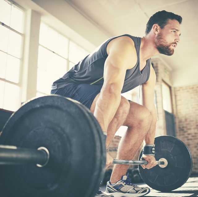 Full length of confident man dead lifting barbell in gym