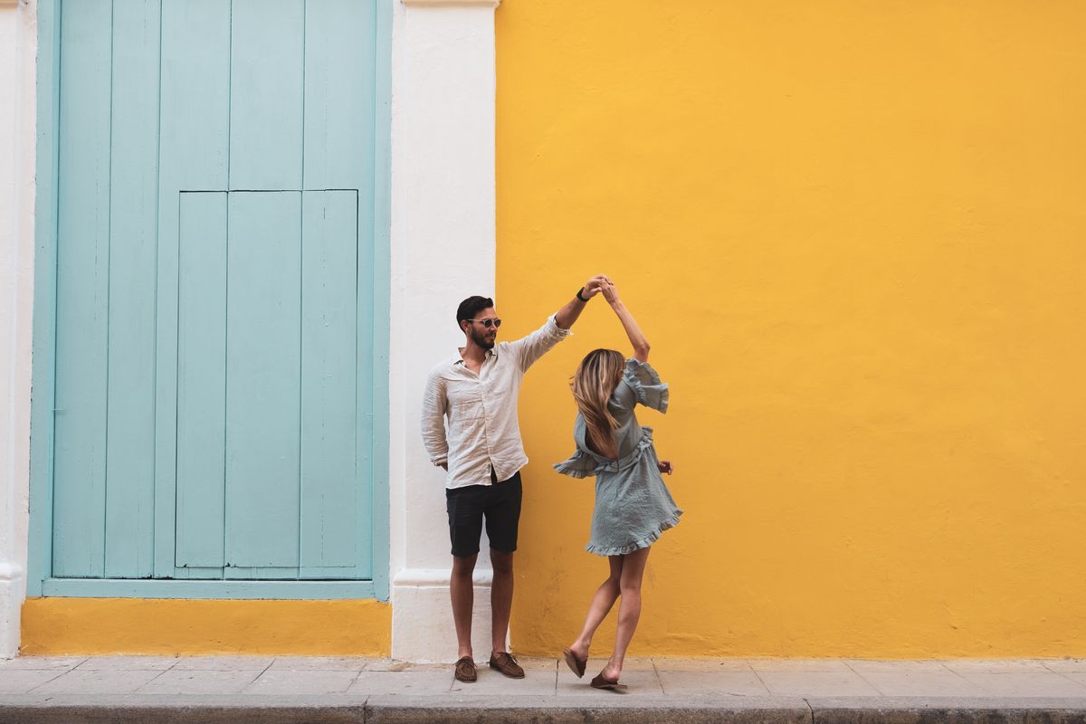 full length of couple dancing on sidewalk against yellow wall