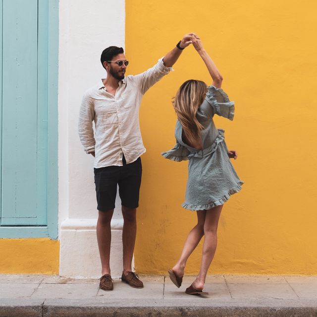 full length of couple dancing on sidewalk against yellow wall