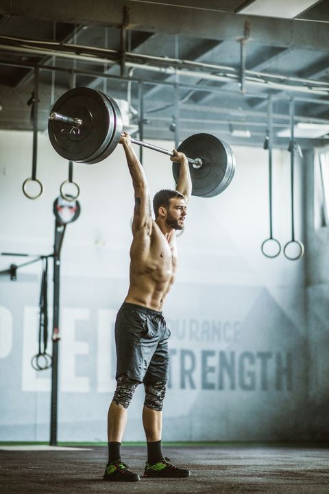 Full length of male athlete exercising strength with barbell in a health club.