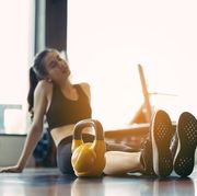 full length of tired young woman sitting with kettlebell in gym