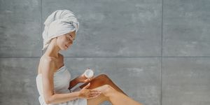 full length of woman wearing towel applying moisturizer in bathroom