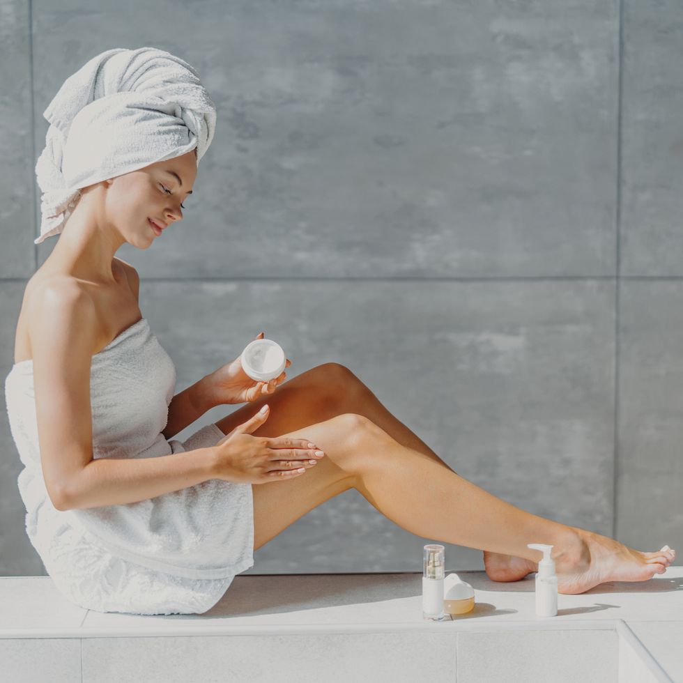 full length of woman wearing towel applying moisturizer in bathroom