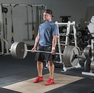full length of young man lifting barbell in gym