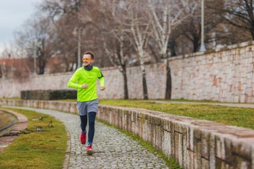 full length shot of a young male runner wearing vibrant running clothes while running in rainy and overcast weather