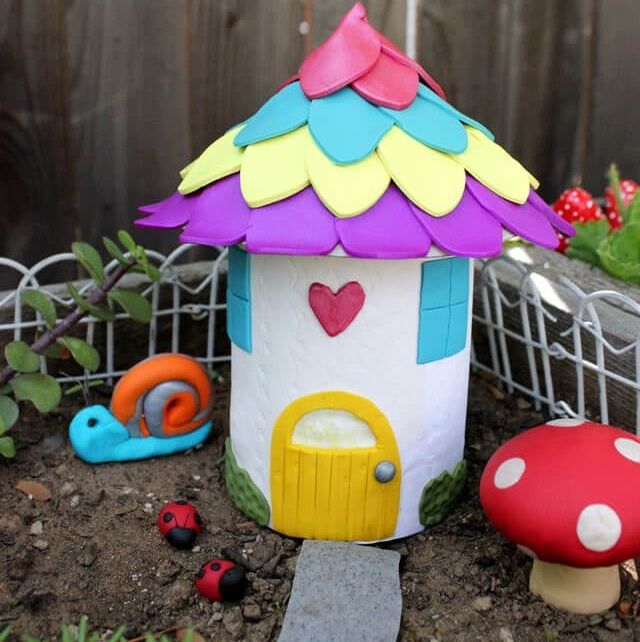 a clay fairy house sits in the corner of the garden
