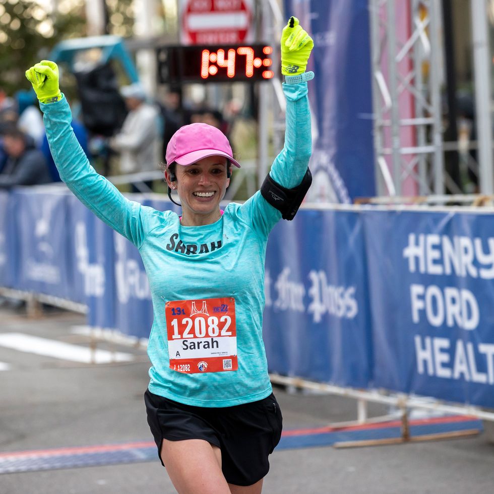 a runner in the detroit free press international half marathon raises her hands as she crosses the finish line