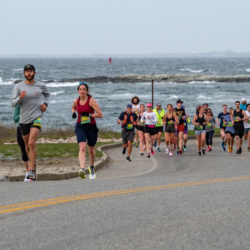 runners crest a hill in the newport half marathon with ocean waves in the background