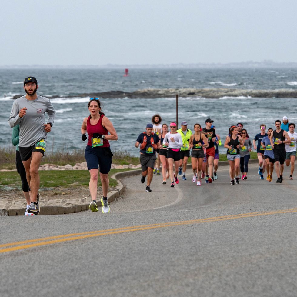 runners crest a hill in the newport half marathon with ocean waves in the background