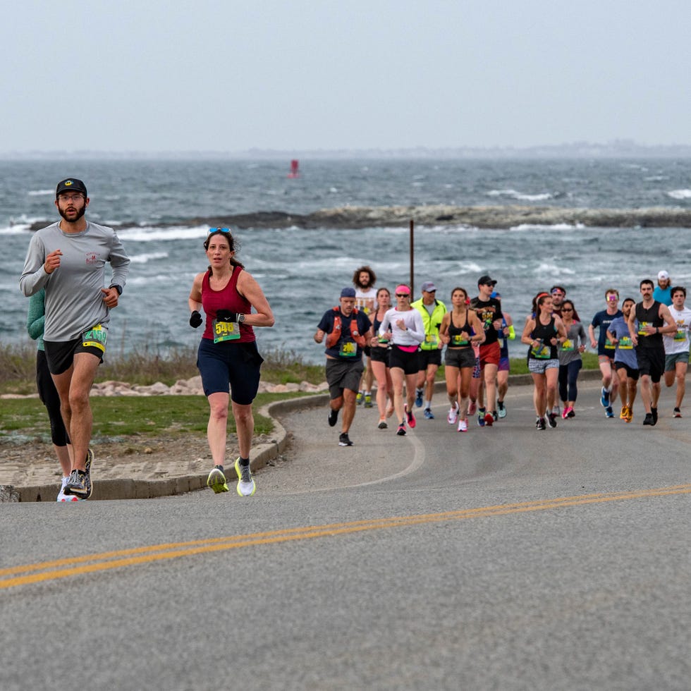 runners crest a hill in the newport half marathon with ocean waves in the background