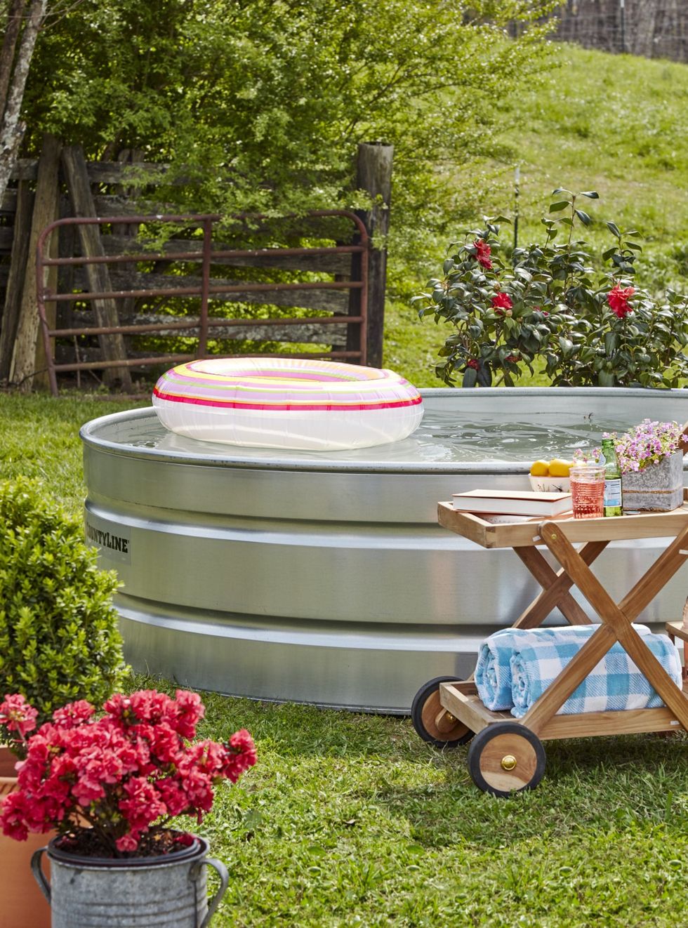 A stock tank pool in a yard with pool floatie and cart to the side with drinks and towels
