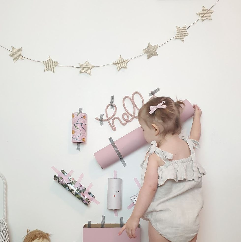 a toddler drops a pom pom into a series of cardboard tubes and containers taped to the wall
