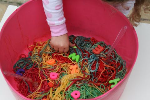 a toddler hand reaches into a bucket of rainbow noodles with toys hidden in it