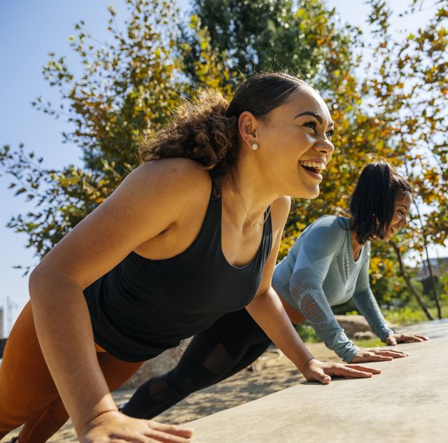 two women doing push ups on ledge outside with greenery and blue skies