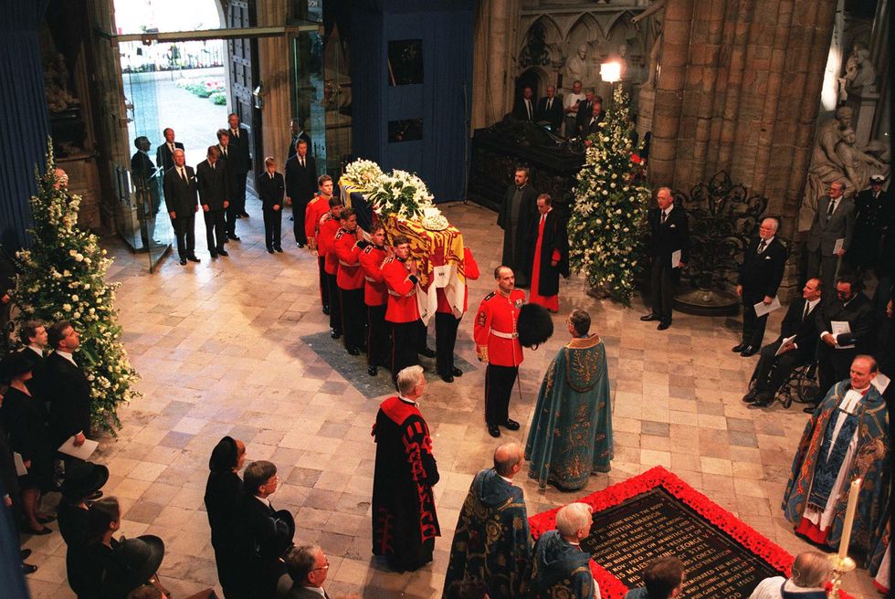 the interior of westminster abby, with several people in formal attire carrying a coffin adjourned with flowers, while many other spectators watch