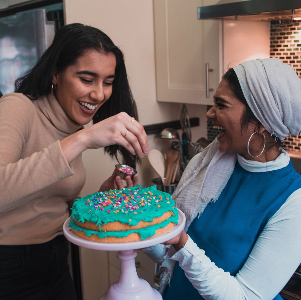 two friends laughing while putting sprinkles on a cake