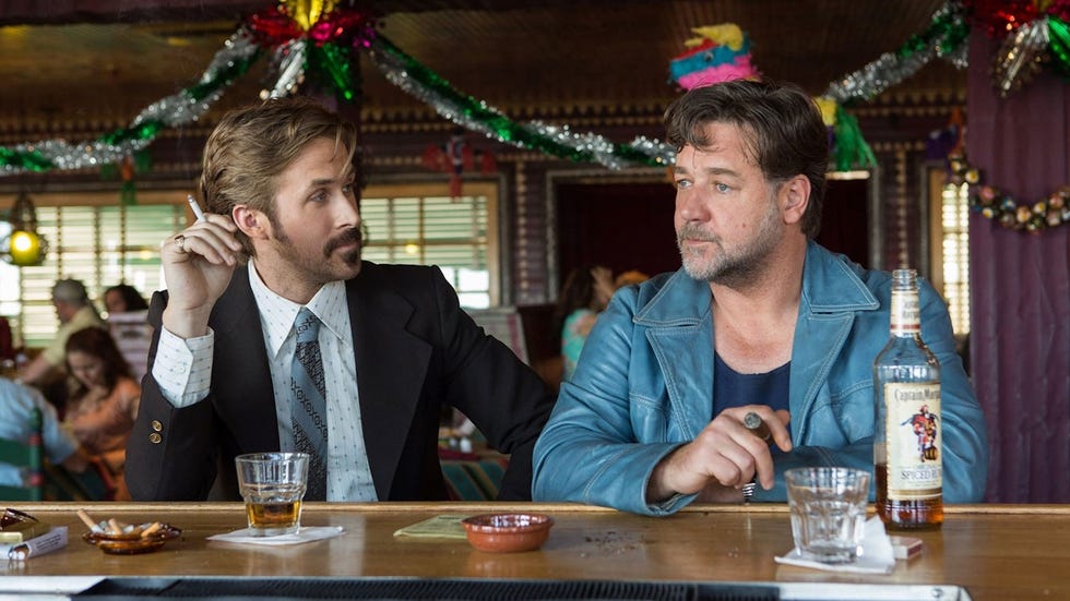 ryan gosling sits at a festive bar wearing a suit in a scene from the nice guys