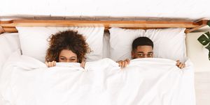 Funny couple hiding under white blanket in bed